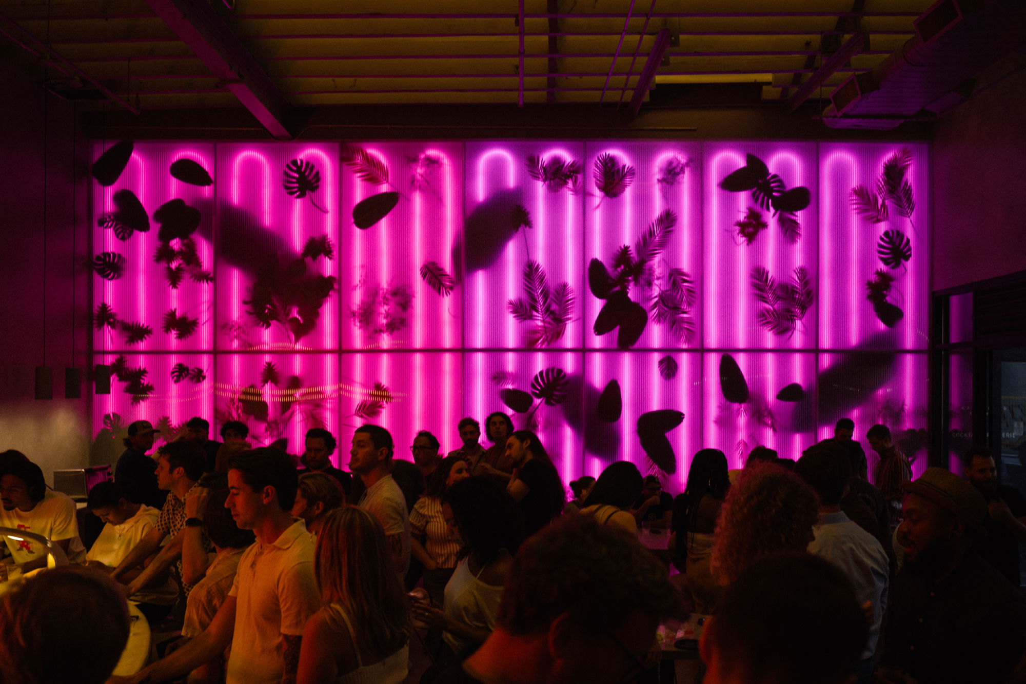 Guests at a Wandering Barman event beneath the signature neon leaf wall